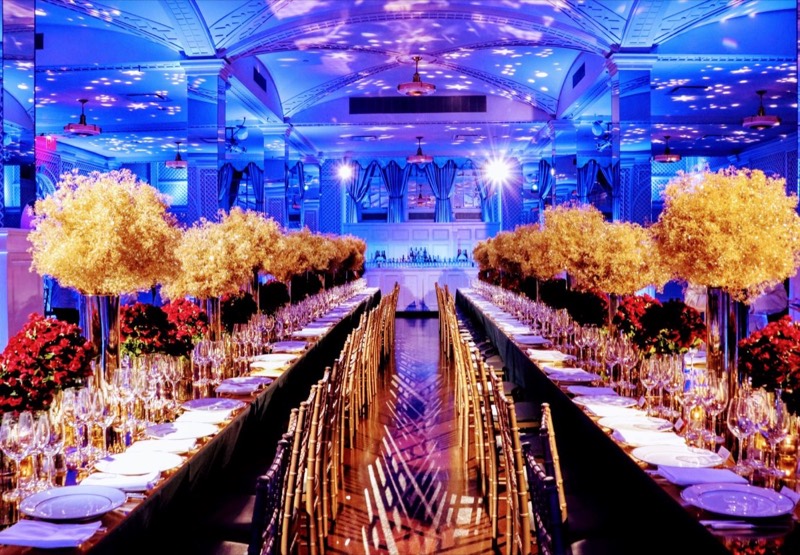 Long banquet table with gold centerpieces running down the Arcade under blue light
