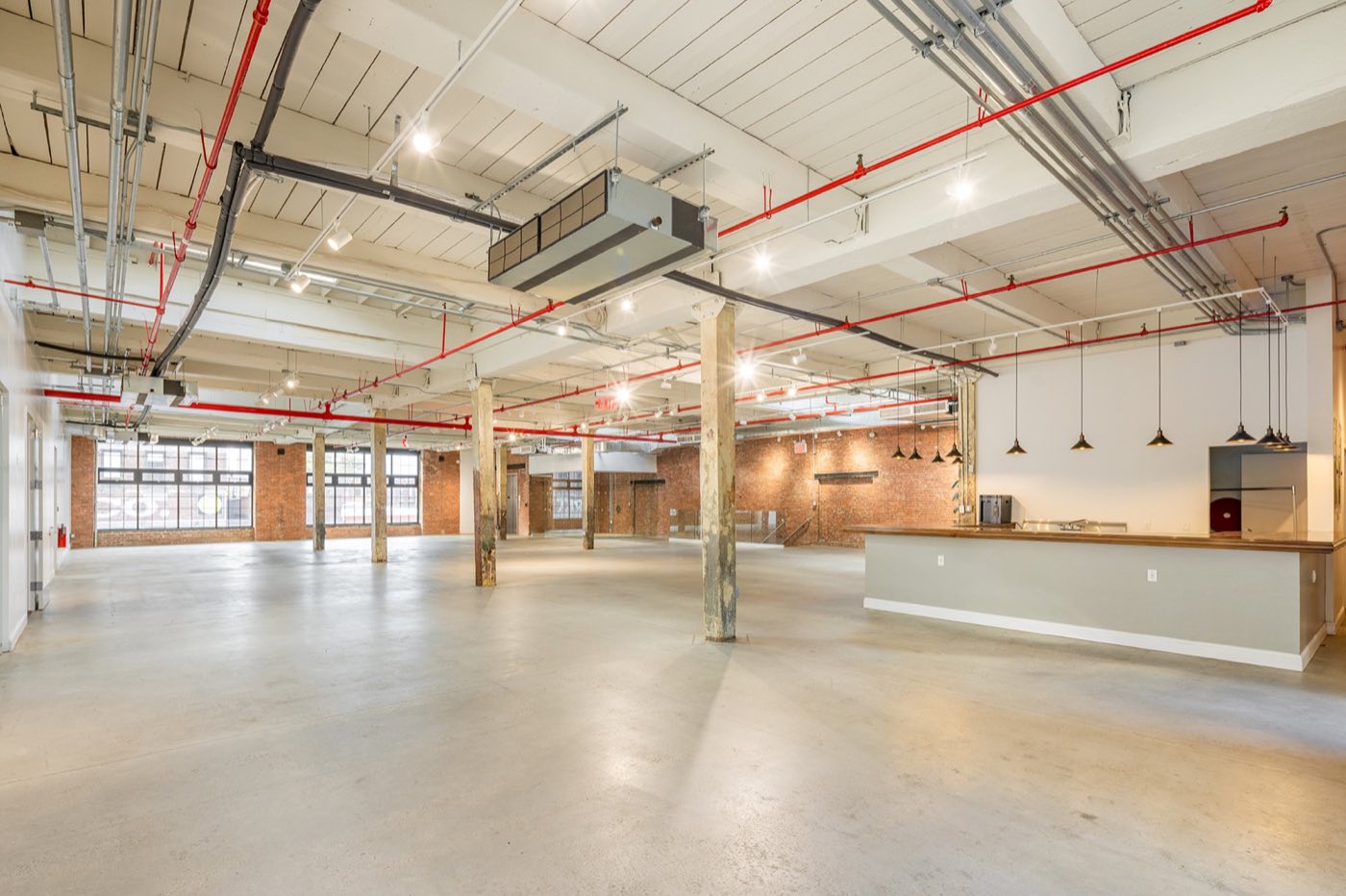 Empty main loft with concrete floor, timber columns, brick walls and a long bar
