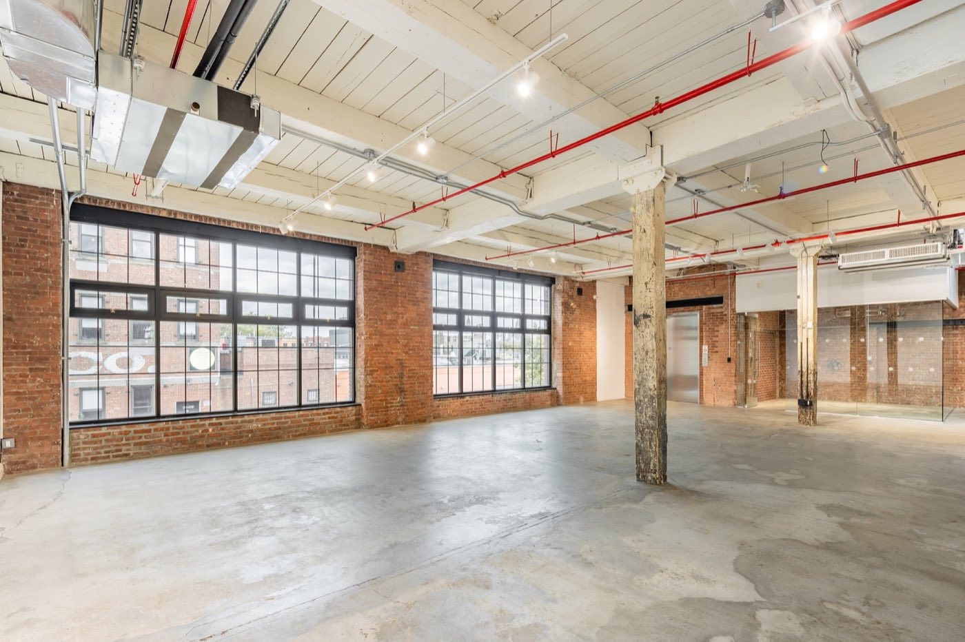Open loft floor with tall factory windows along an exposed brick wall