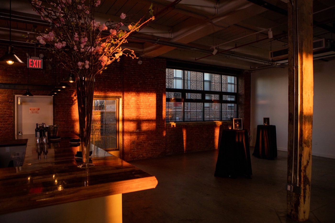 Loft bar and cocktail tables lit by sunset light through factory windows