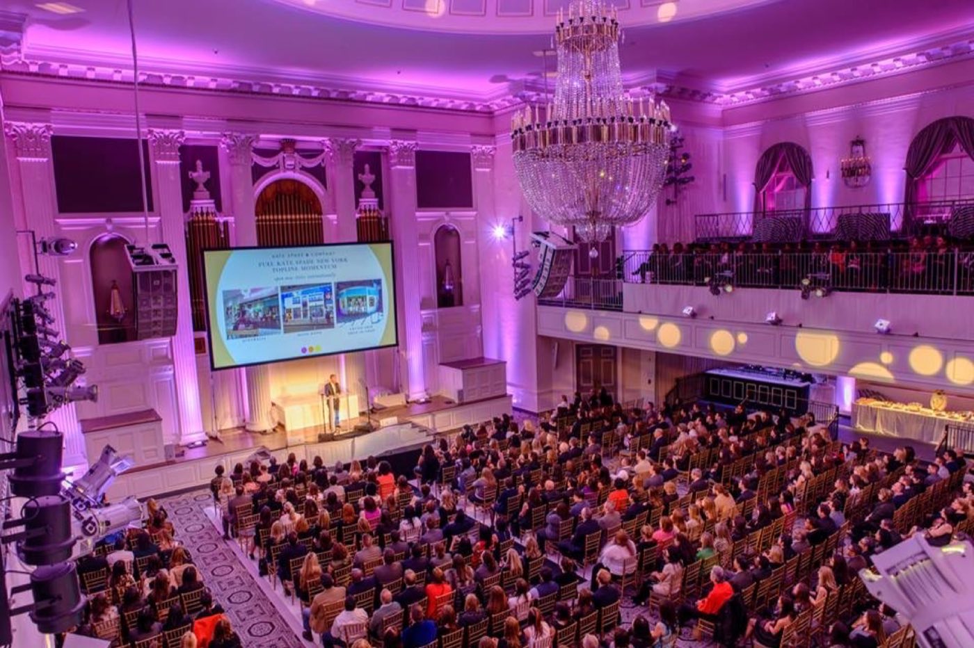 Ballroom in theater seating facing a stage with screen and wraparound balcony