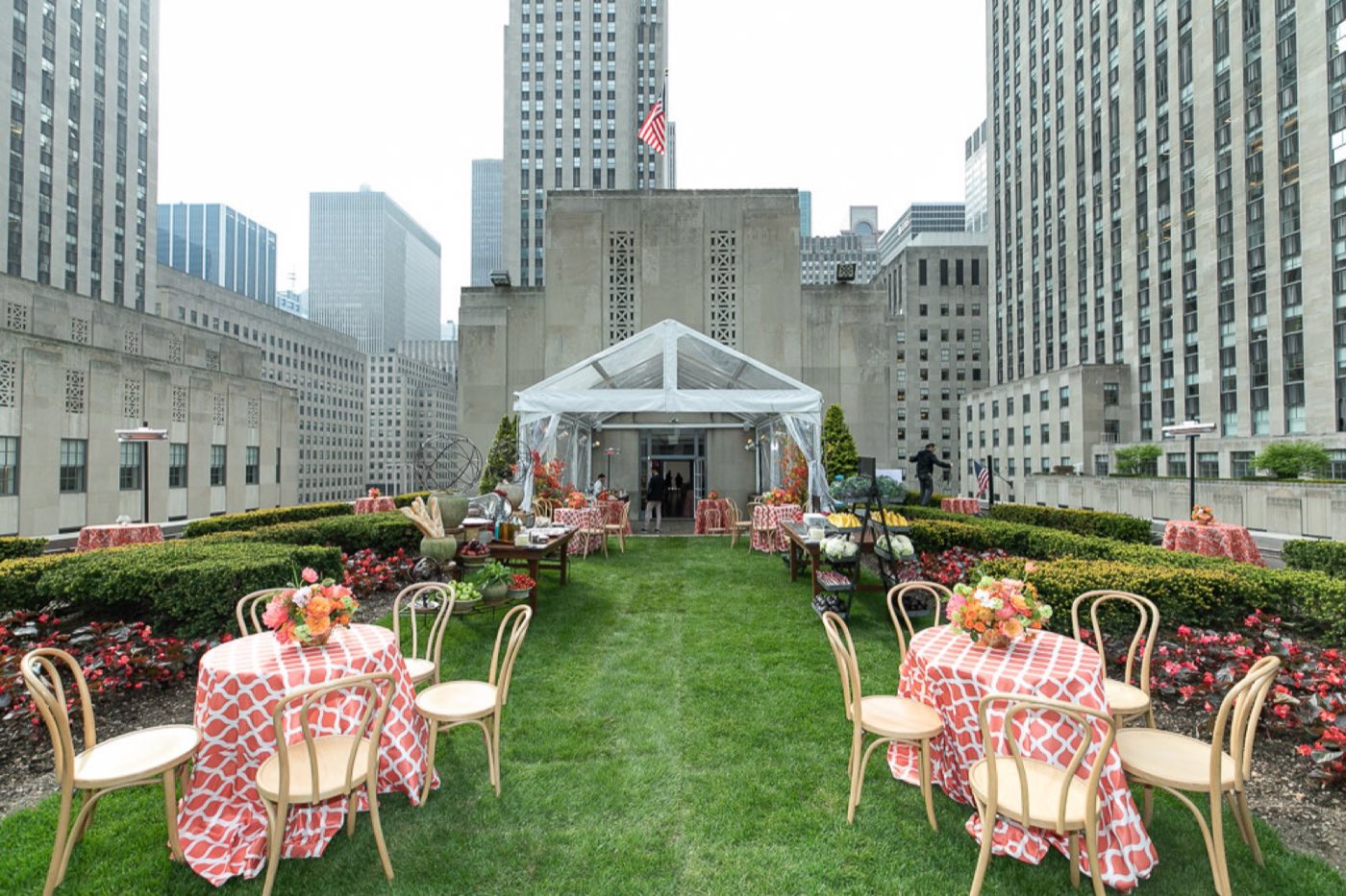 Rooftop garden lawn with hedges and a tent at the far end, framed by Rockefeller Center towers