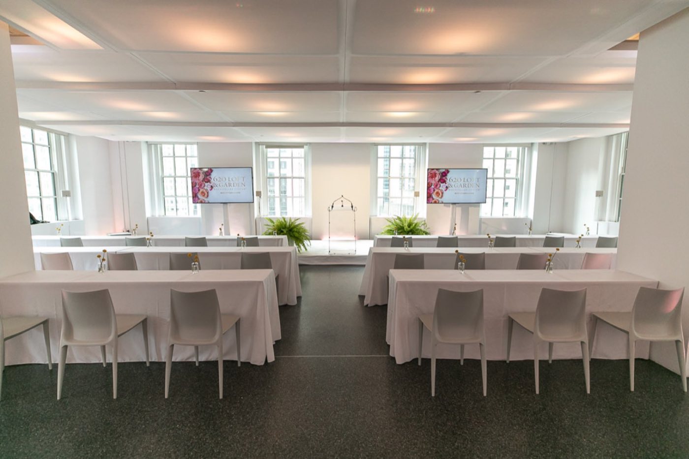 Indoor loft set classroom style with white tables, tall windows and two screens