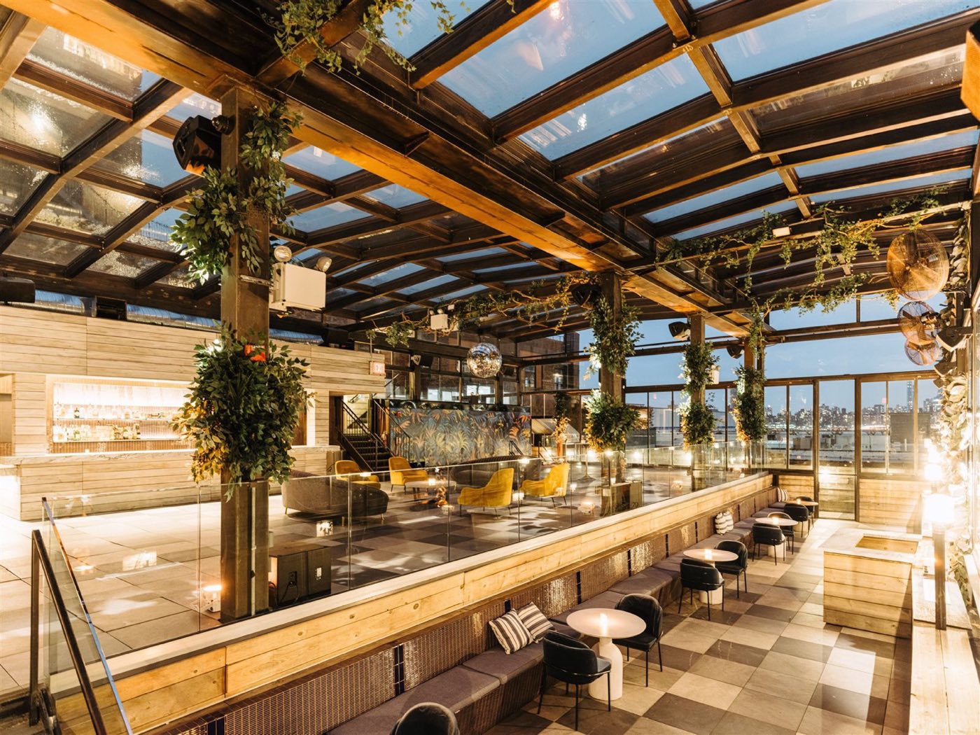 Rooftop bar under a retractable glass roof with plants and skyline views