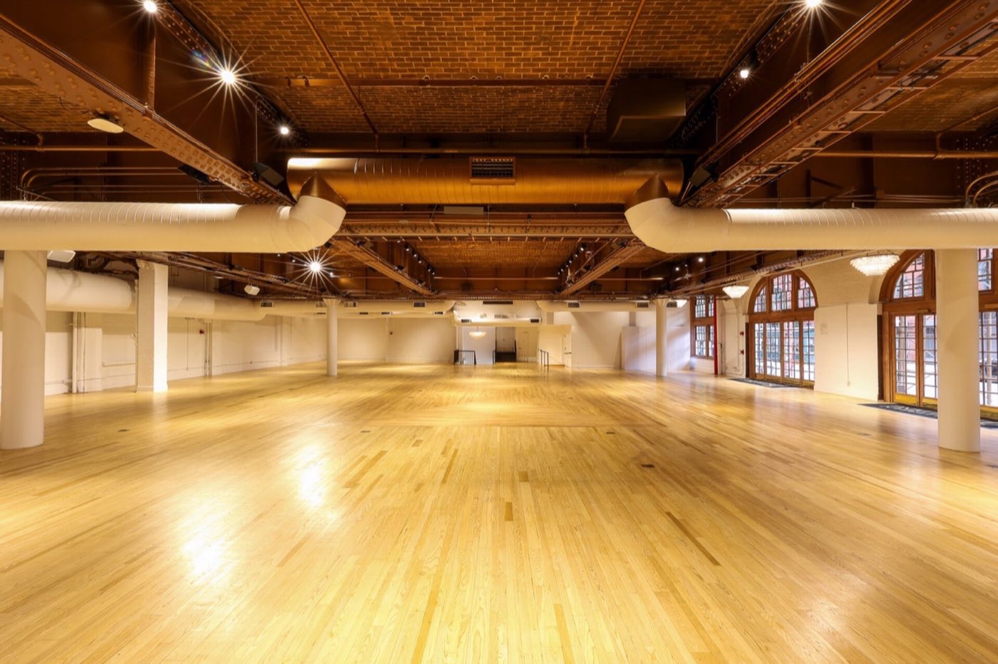 Empty main floor with maple floors, arched windows and exposed ceiling