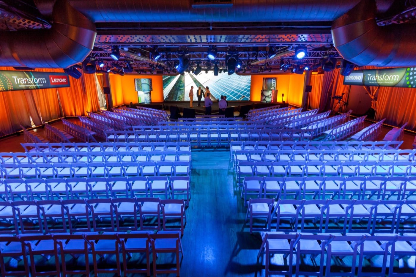 Main floor set theater style with blue lighting and a stage with screens