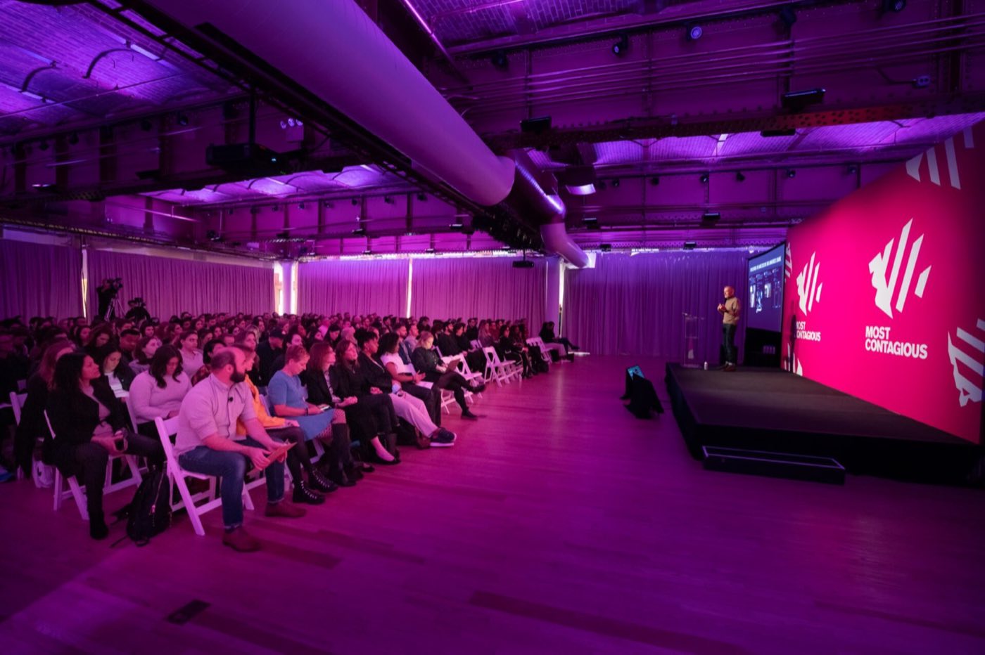 Conference session with seated audience facing a stage in purple light