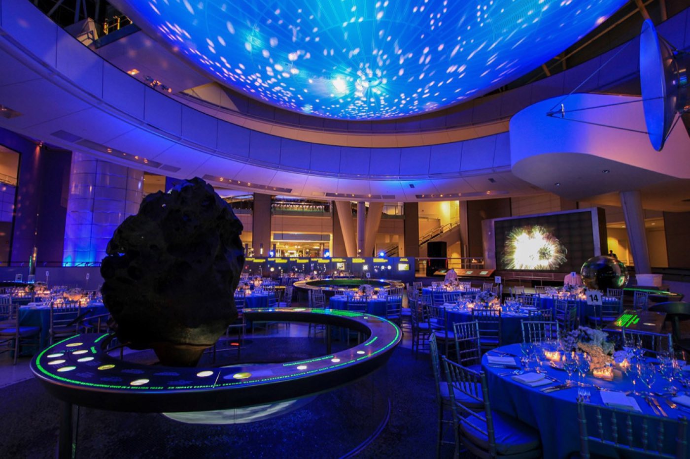Hall of the Universe set with round dinner tables under a projected star ceiling