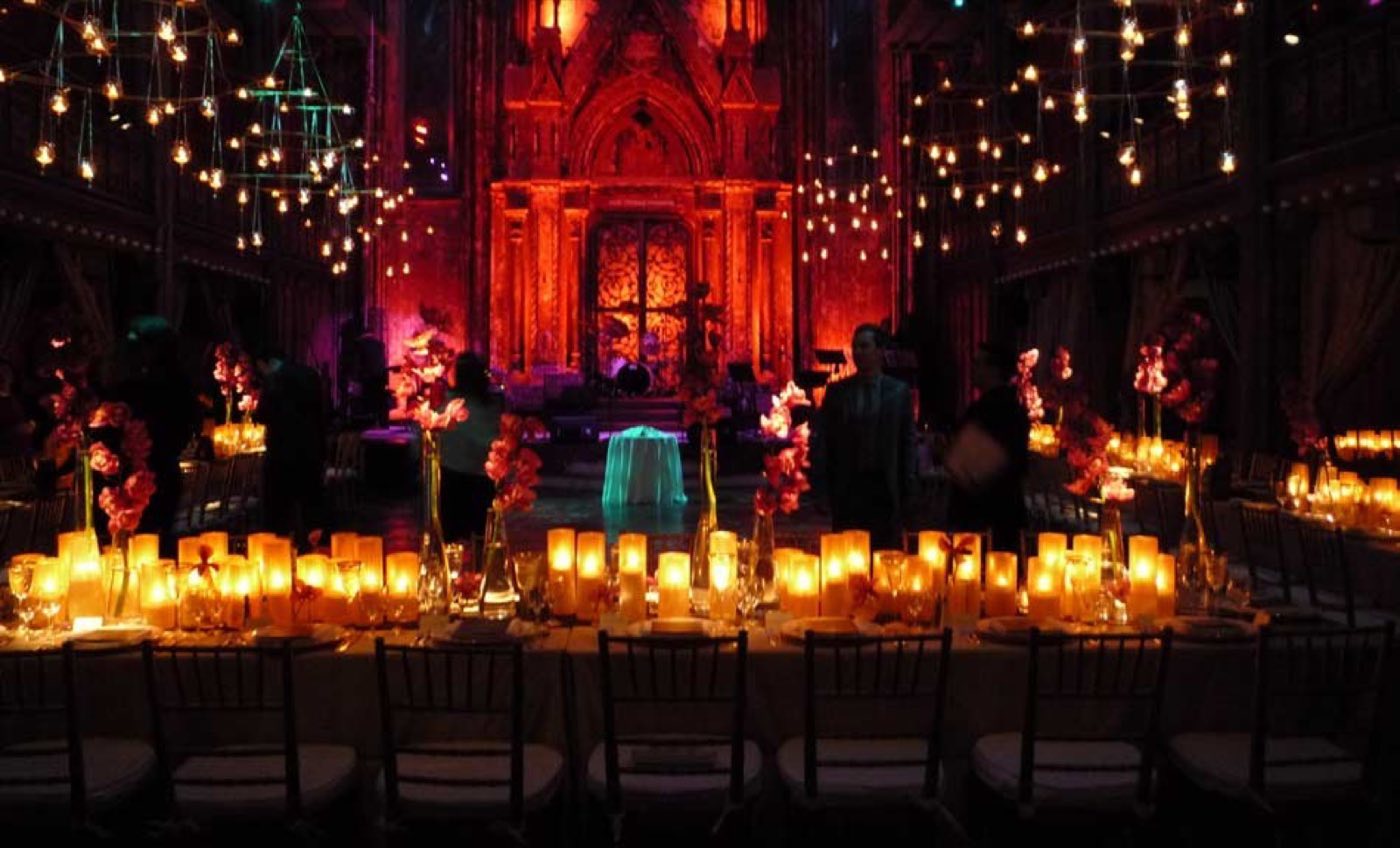 Long candlelit tables under string lights with a red-lit altar wall