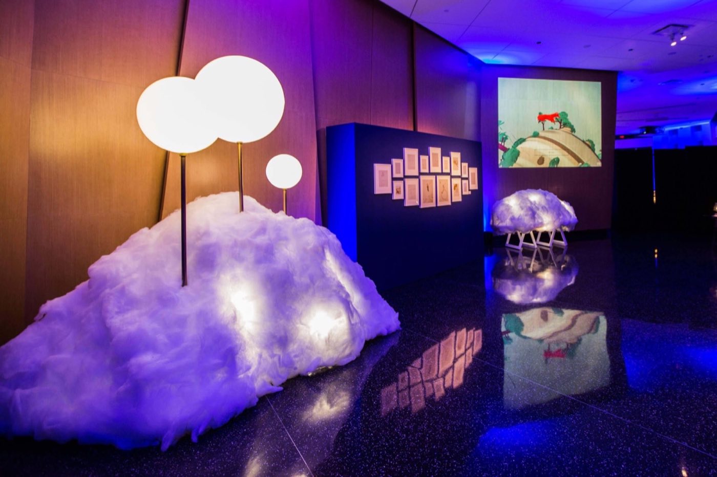 Dimly lit room with a large cloud installation and a projection screen