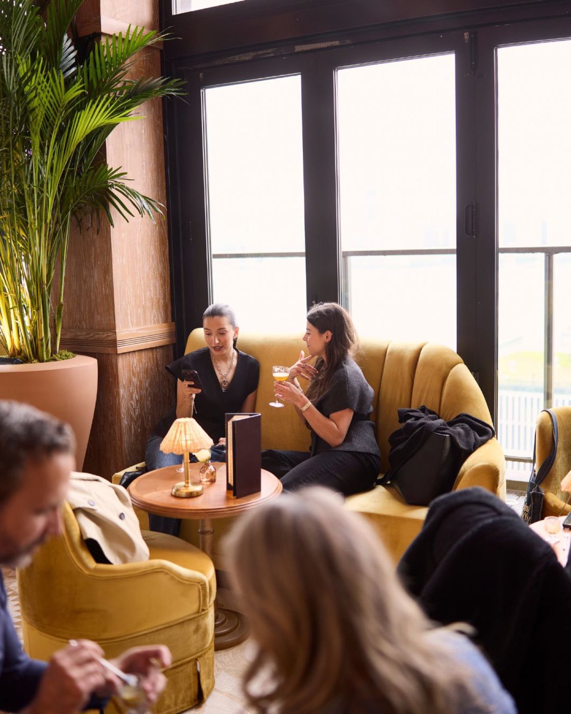 Lounge seating beside tall windows with palms at Bar Hugo