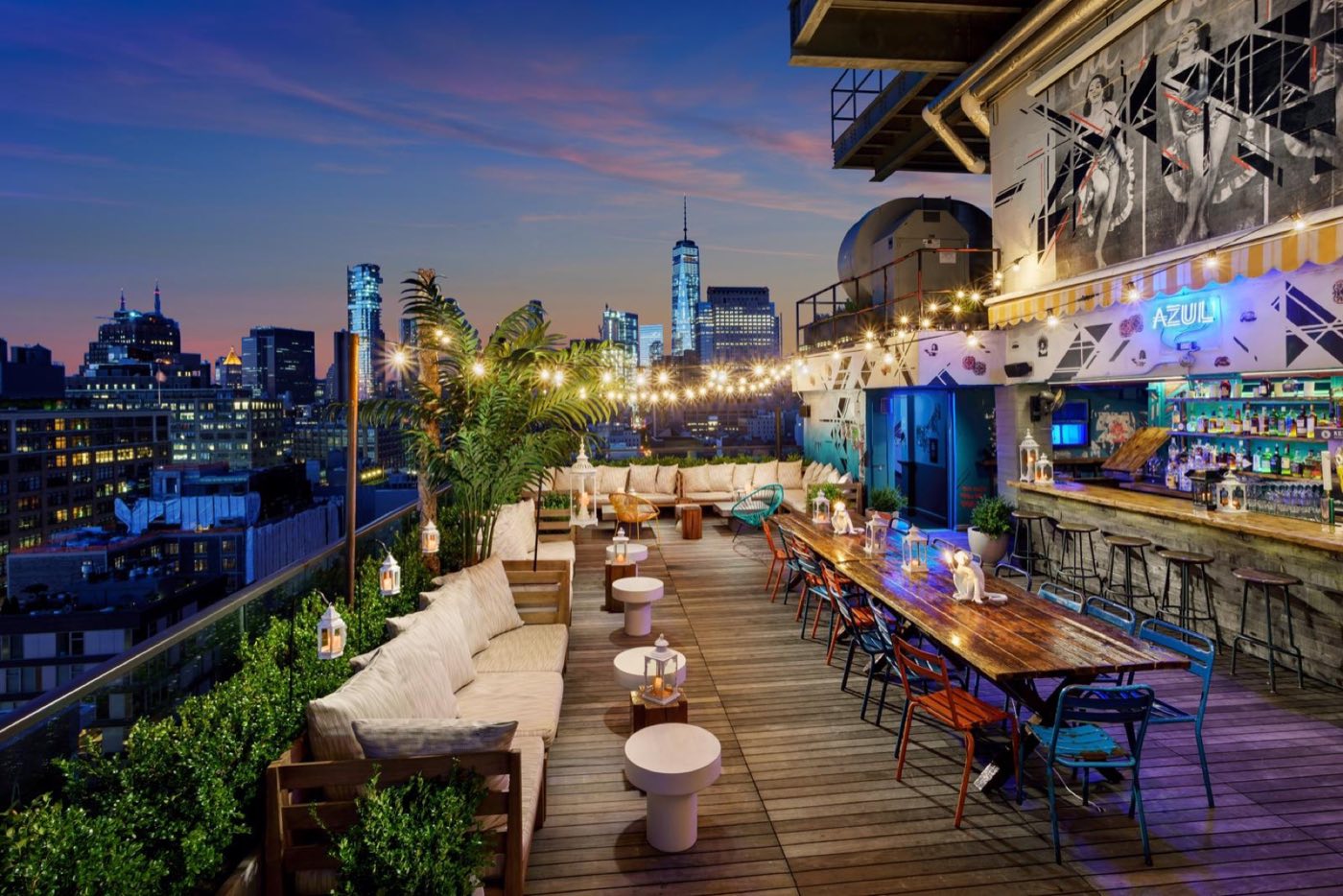 Open-air rooftop bar at dusk with string lights and the downtown skyline