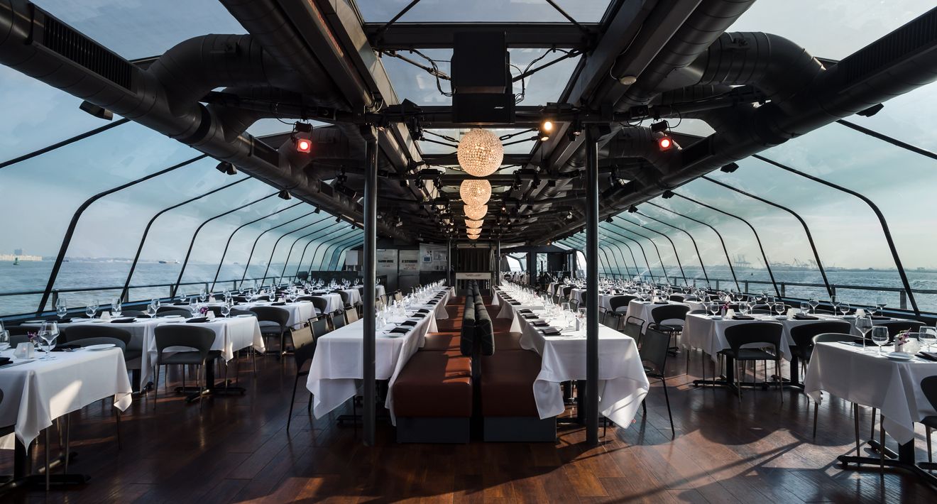 Long glass-roofed dining deck set with white tablecloths and globe chandeliers