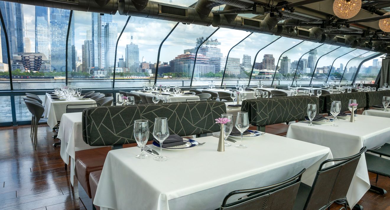 Dining tables beside curved glass walls with Hudson Yards towers outside