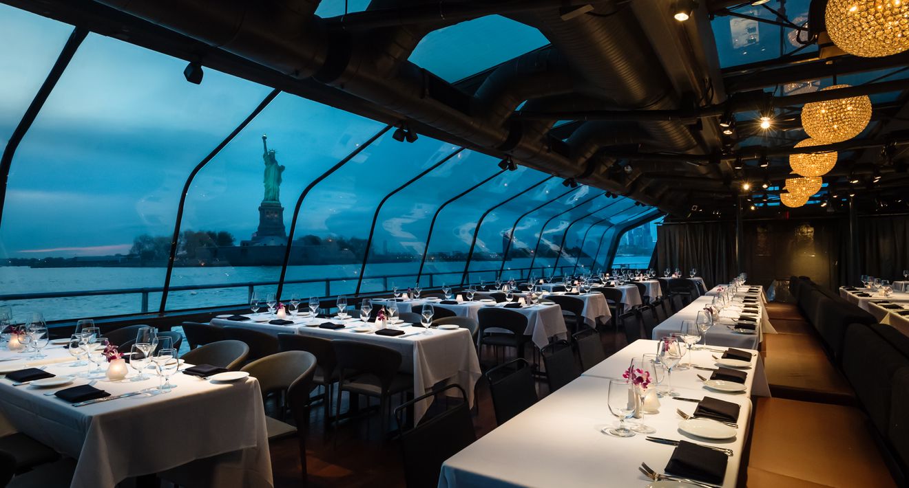 Glass-enclosed dining room at dusk with the Statue of Liberty beyond