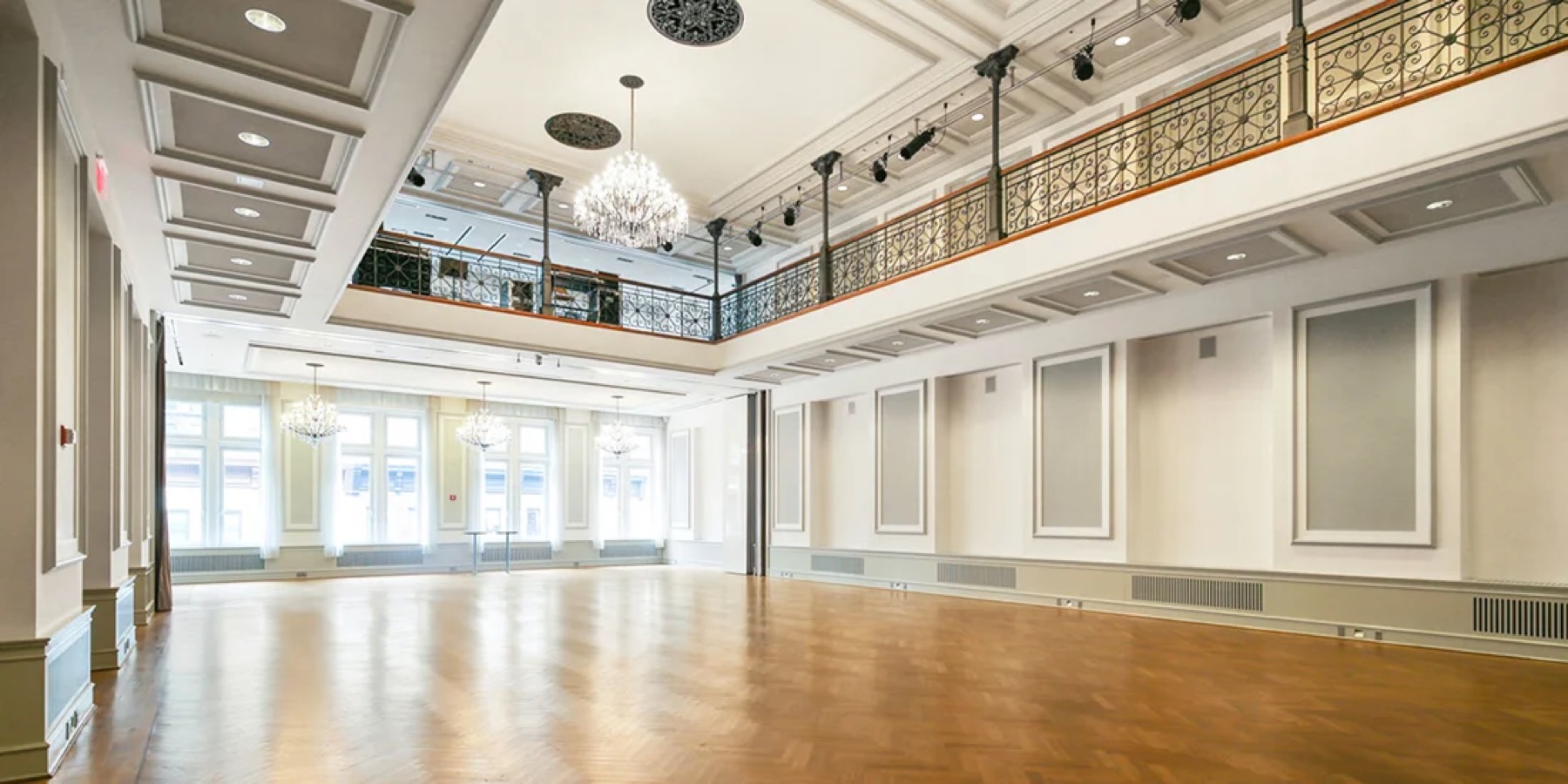 Empty Grand Ballroom with wood floor, tall windows and a balcony around the room