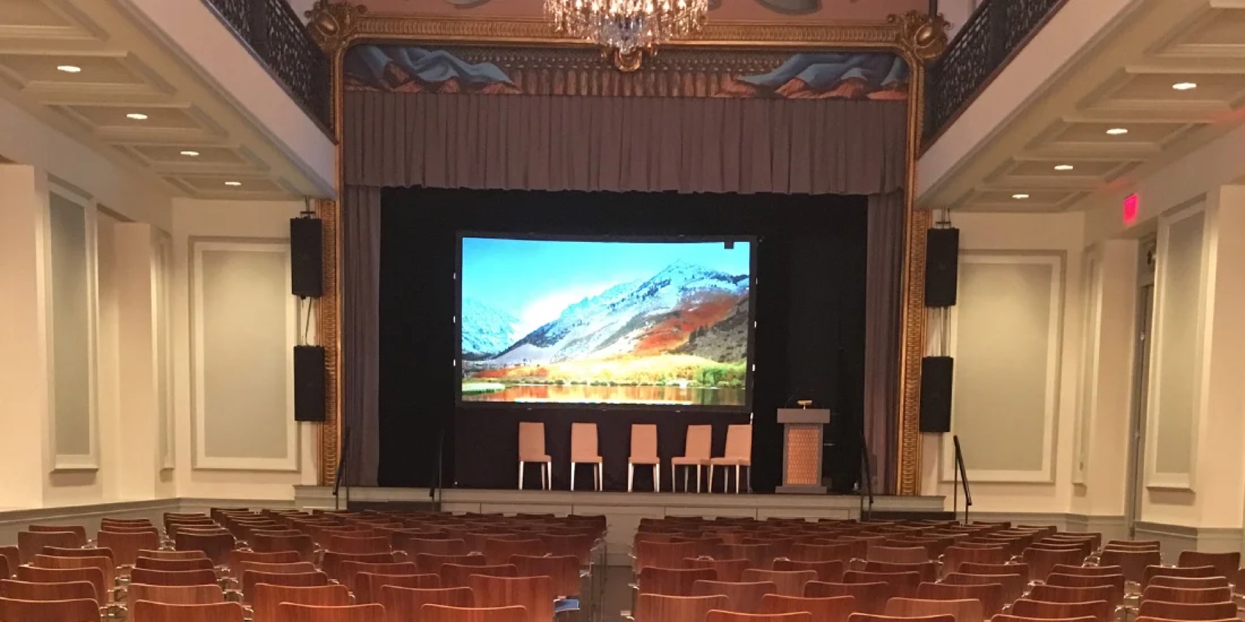 Ballroom set with theater rows facing the stage and a projection screen