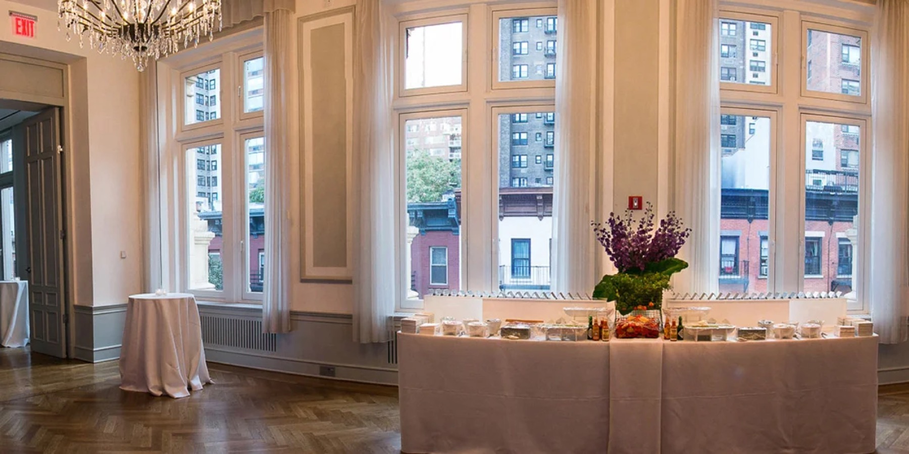 Tall ballroom windows with a buffet table and chandelier for a reception
