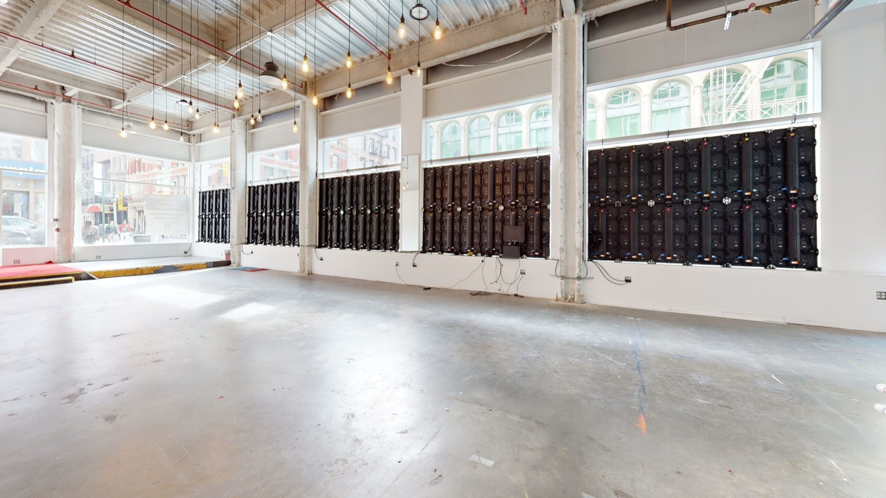 Empty street level retail space with concrete floor, tall windows and hanging Edison bulbs