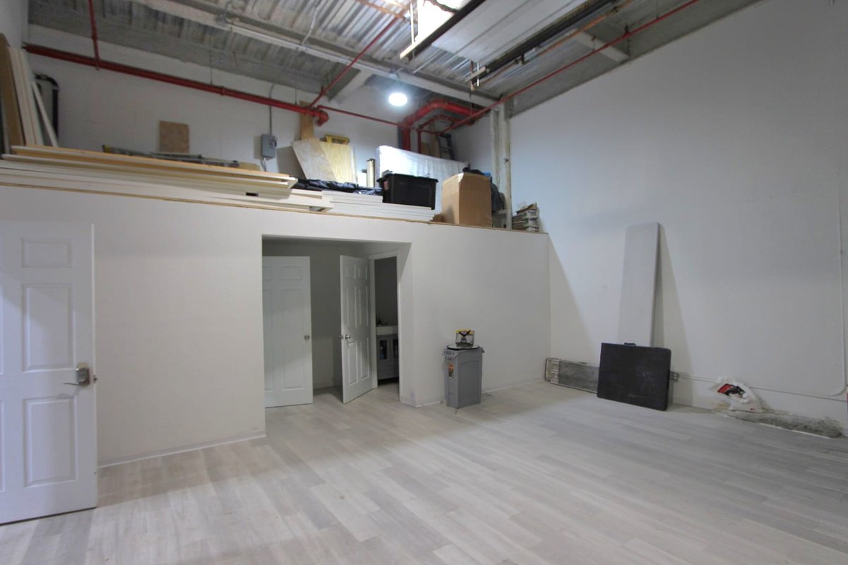 Back of a white retail space with light wood floor, side doors and storage ledge