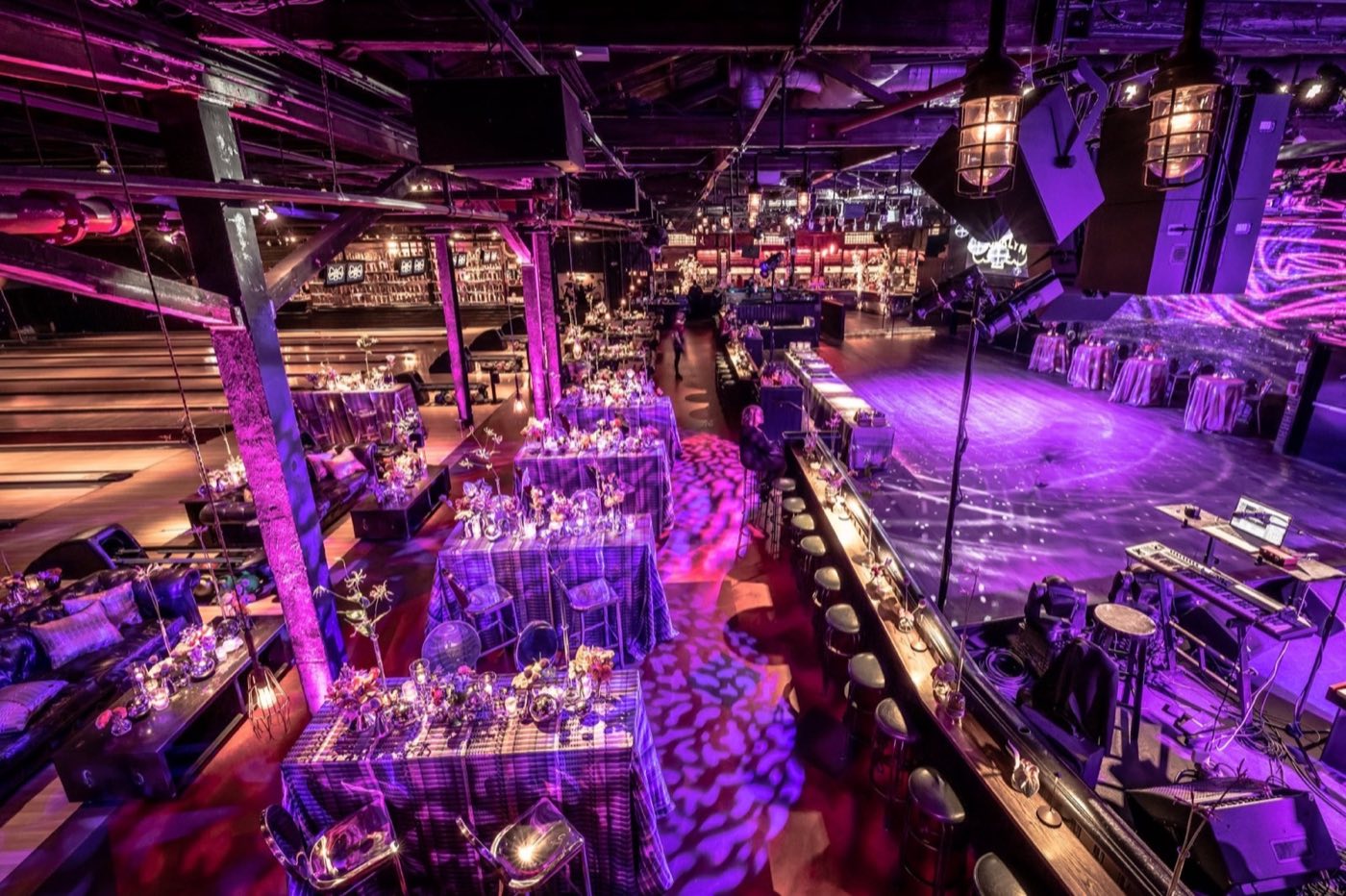 Main room set for a seated dinner with draped tables and purple lighting