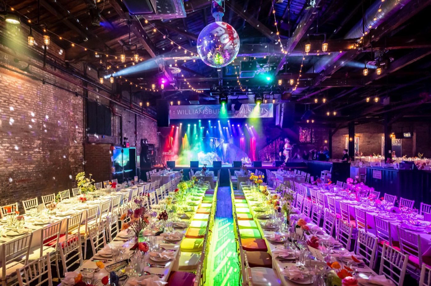 Long banquet tables down the main room facing the lit stage and disco ball