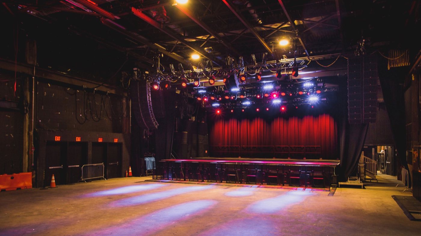 Empty main floor facing the stage, with red curtain, lighting truss and exposed steel beams