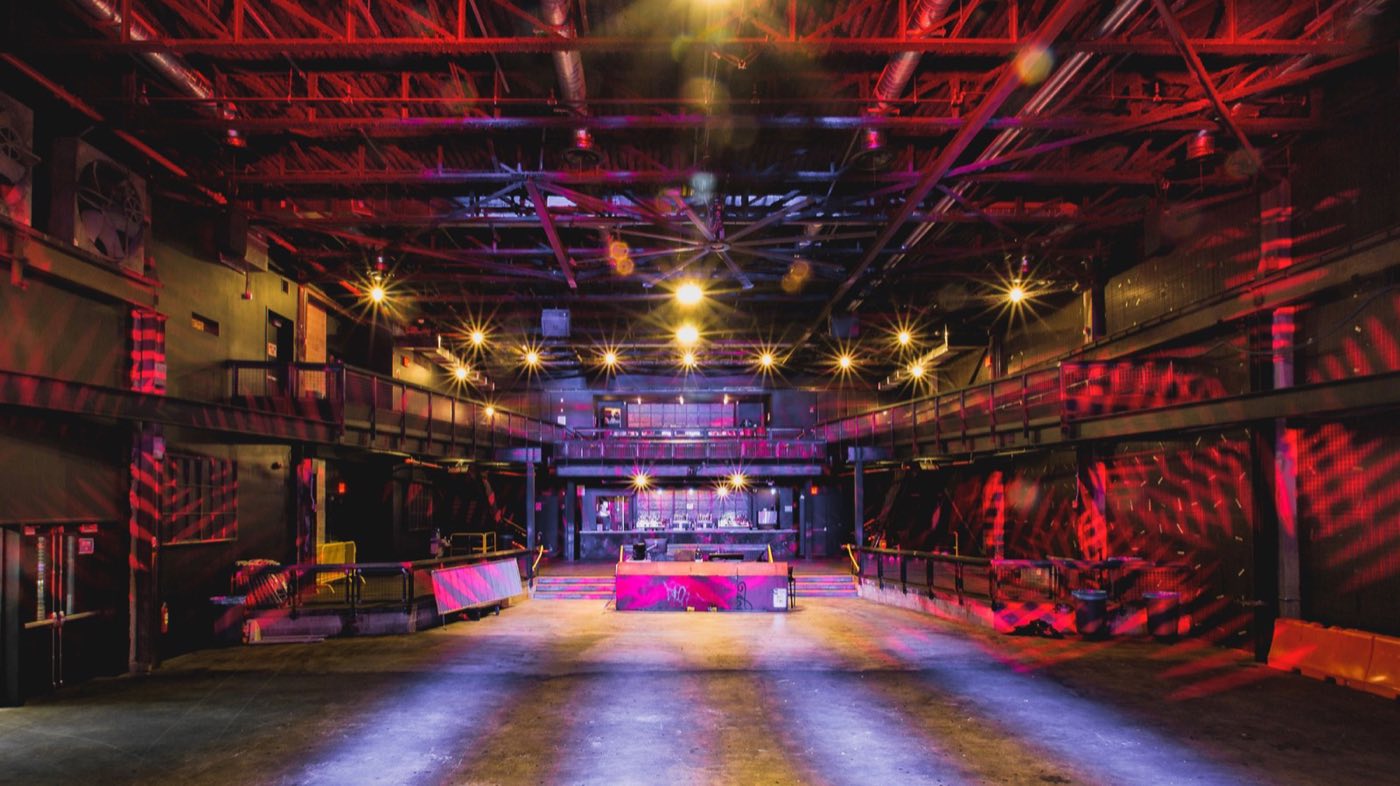 Empty main floor seen from the stage, showing the balcony wrapping the industrial hall
