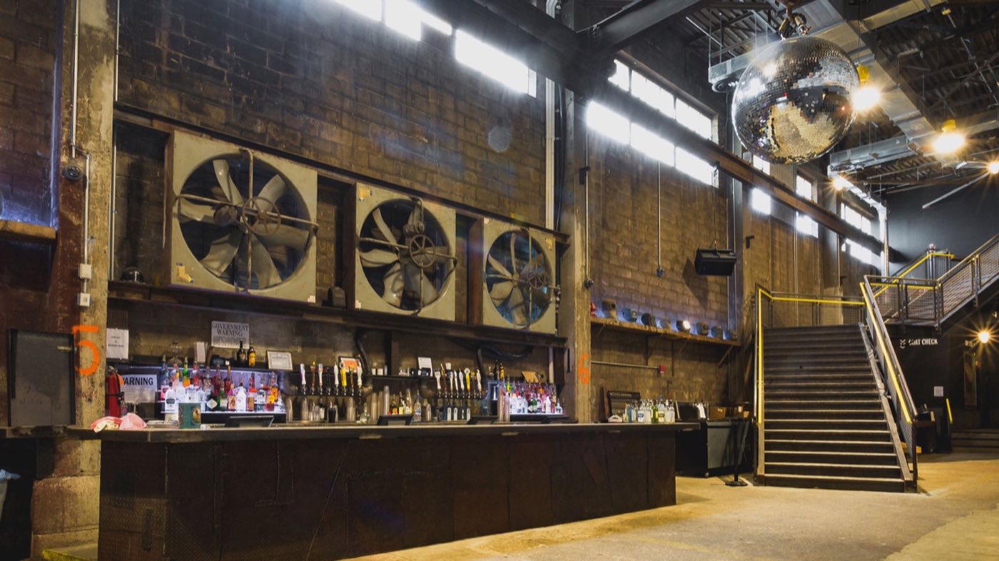 Main-floor bar under the brick wall, industrial fans and staircase to the balcony