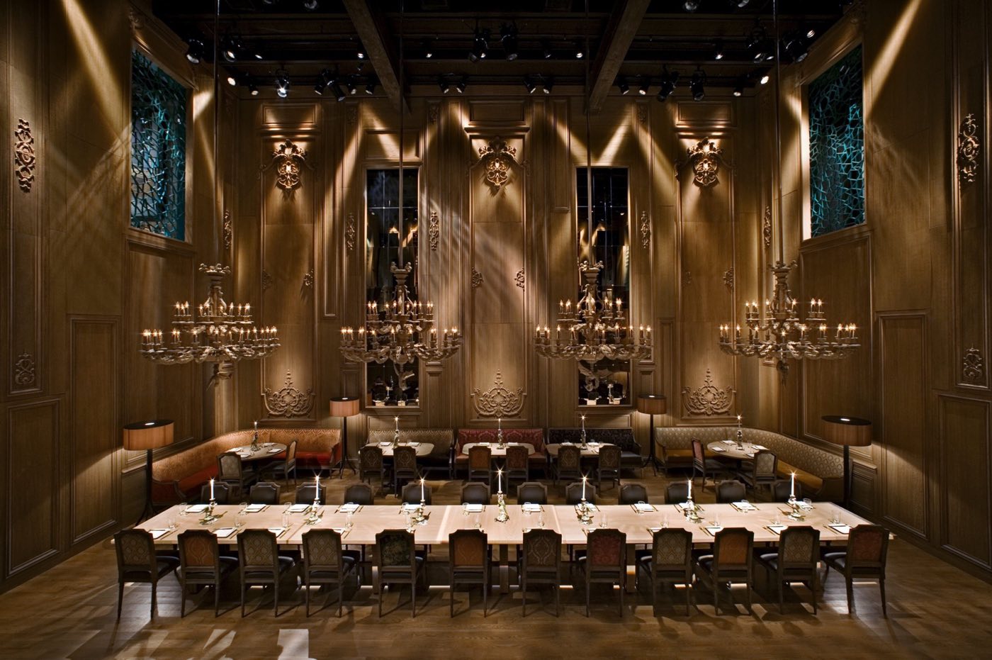 Long banquet table under rows of chandeliers in a carved wood hall