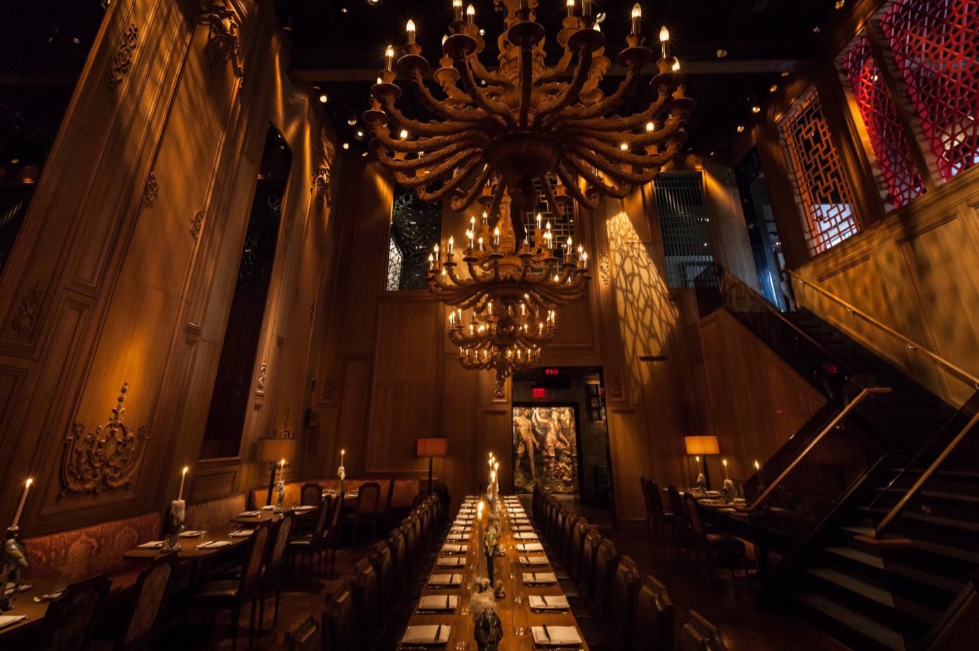 Candlelit hall with chandeliers and a long communal table seen from above