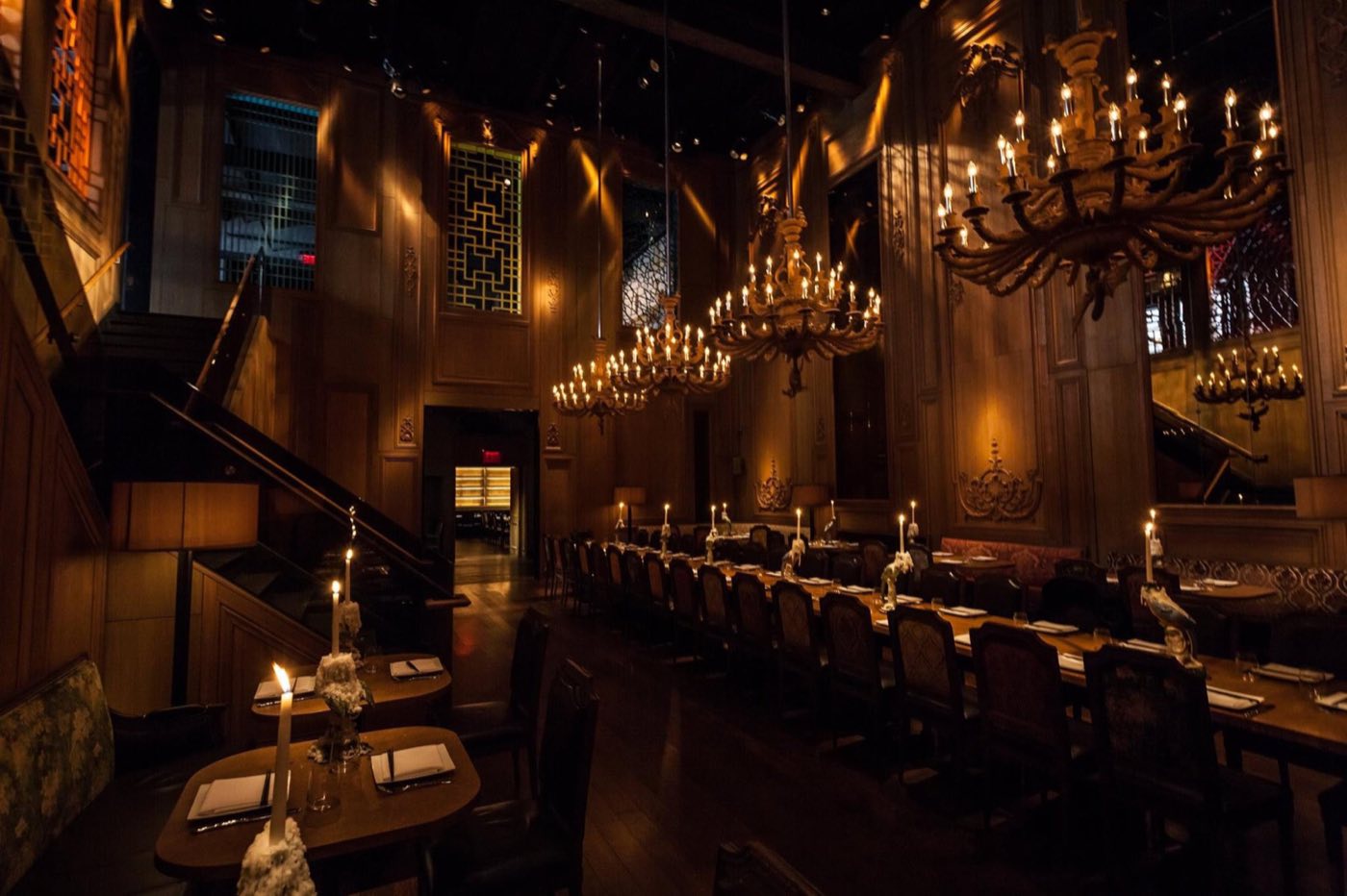 Lower-level hall with chandeliers, a staircase and tables set for dinner