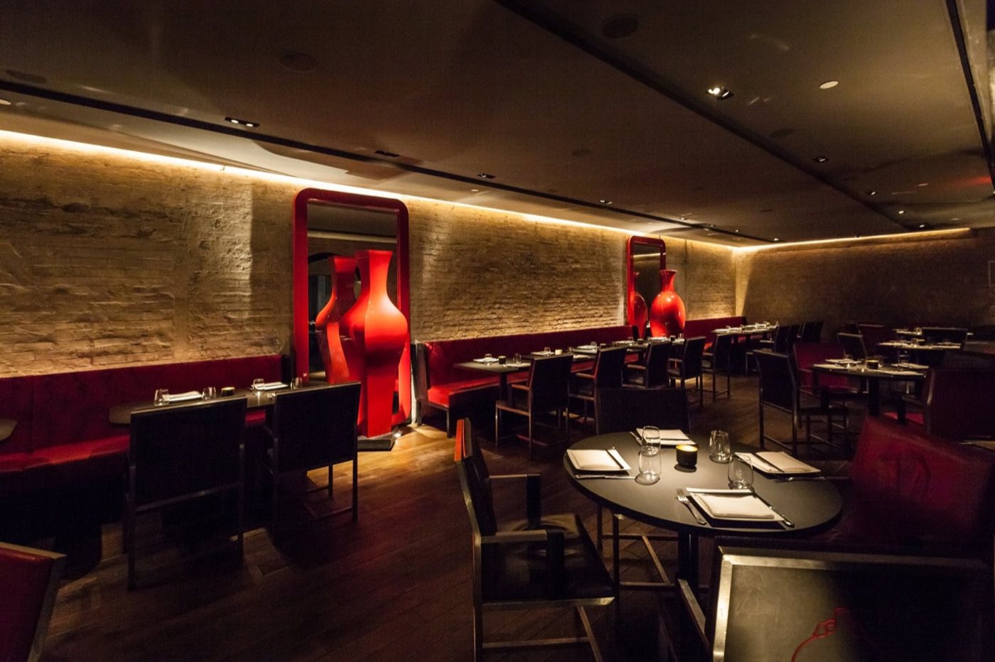 Dining room with red banquettes, tall red vases and set round tables
