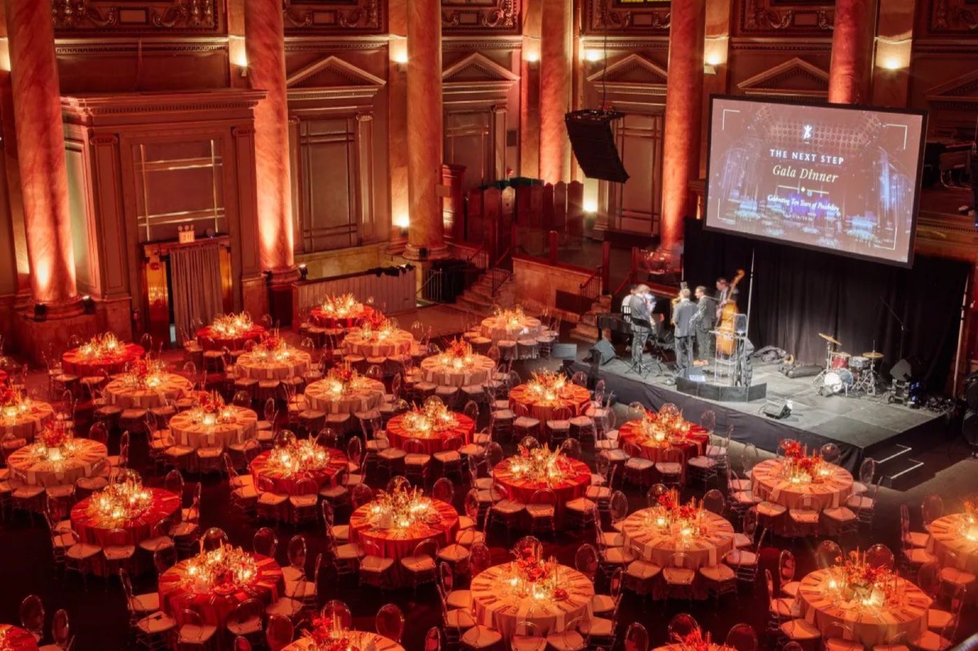 Gala dinner in the ballroom with a stage, screen and warm uplit columns