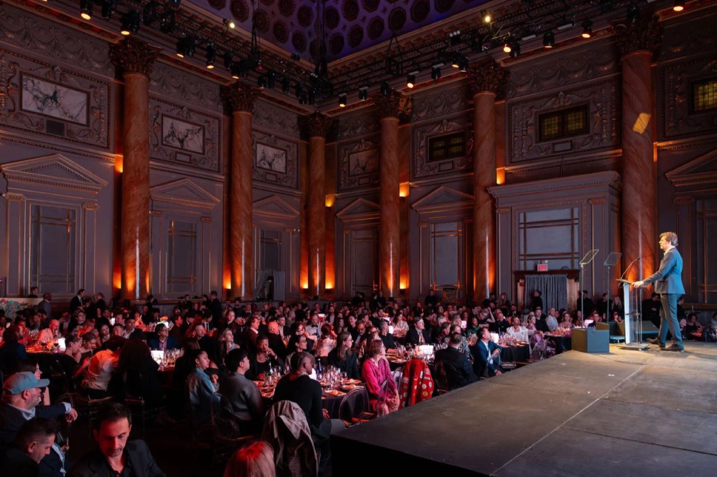 Speaker on stage addressing a full seated audience in the ballroom