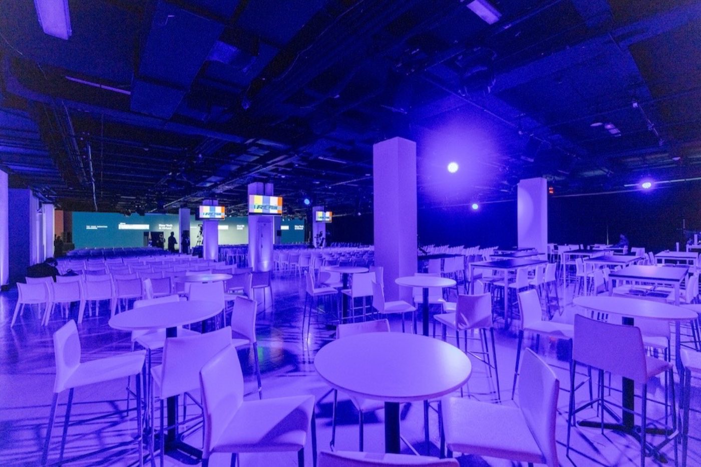 Open floor set with cafe tables and high tops under blue lighting