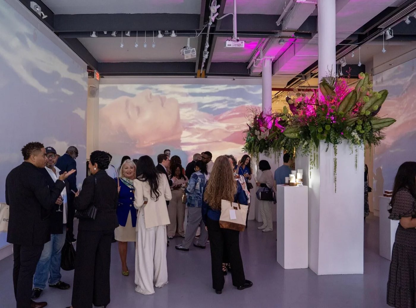 Reception in a white gallery with sky projections on the walls and tall floral columns