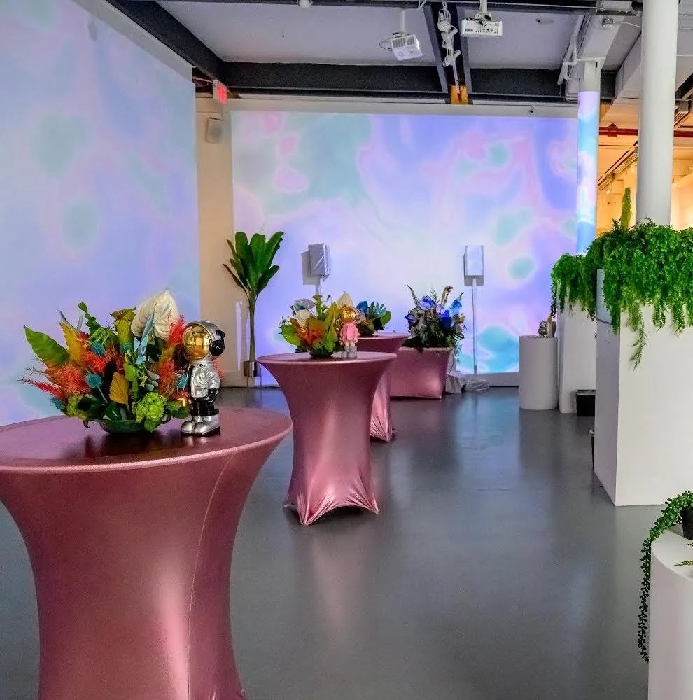 Pink cocktail tables and greenery in front of a pastel projection on the back wall