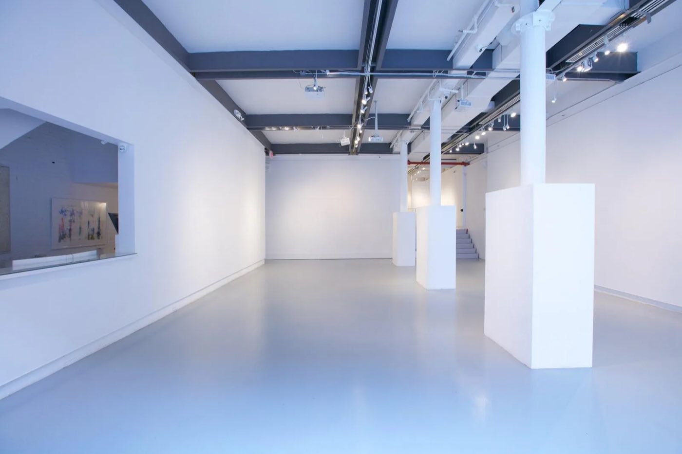 Empty white gallery with columns, polished gray floor and track lighting
