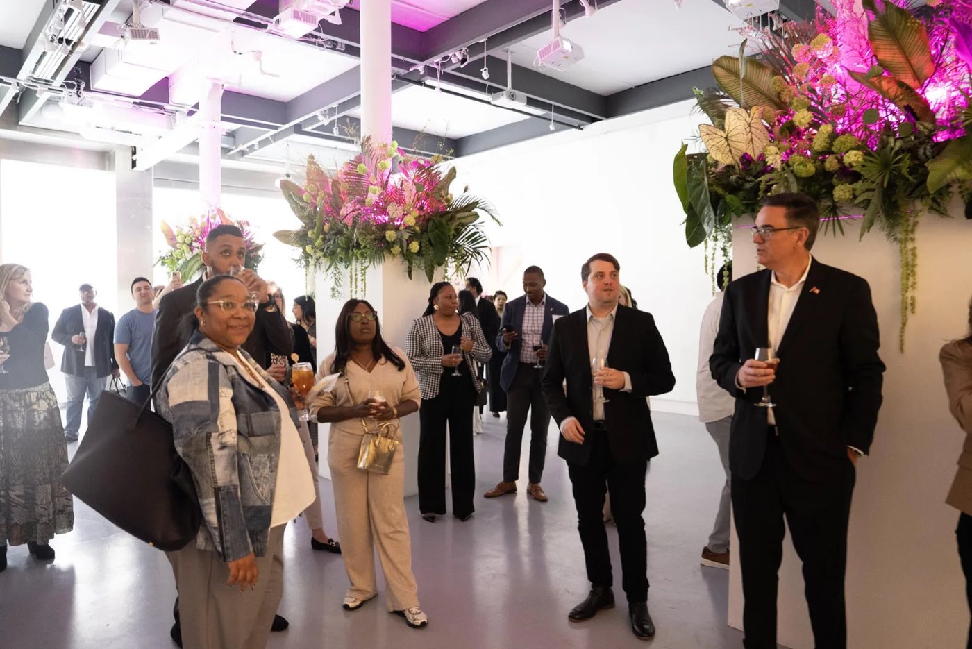Guests with drinks among tall floral displays in a bright white gallery