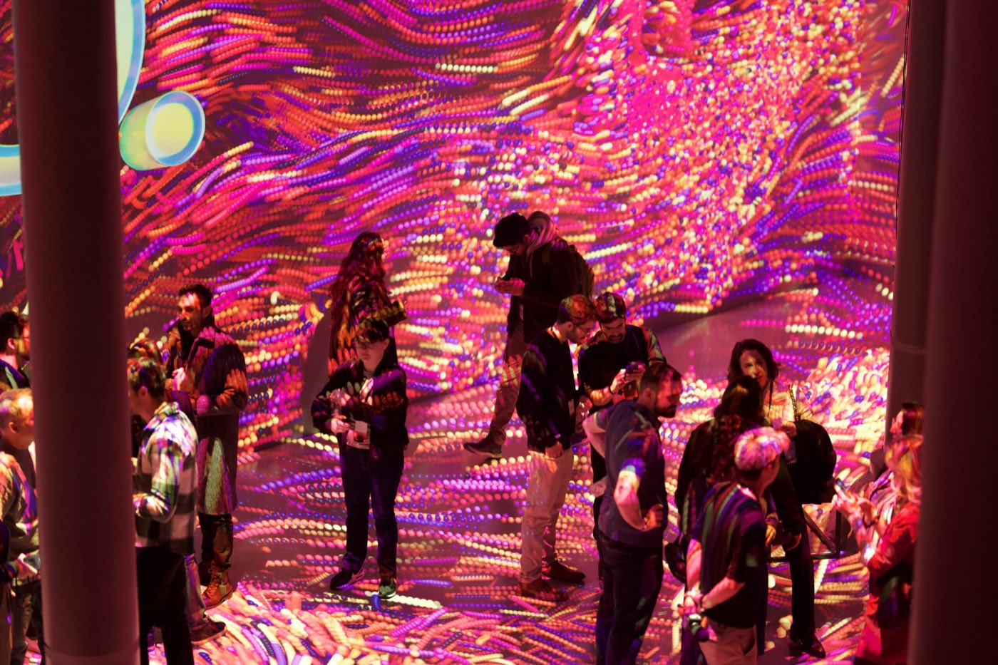 Guests standing on a floor covered in pink and orange projected light between steel columns
