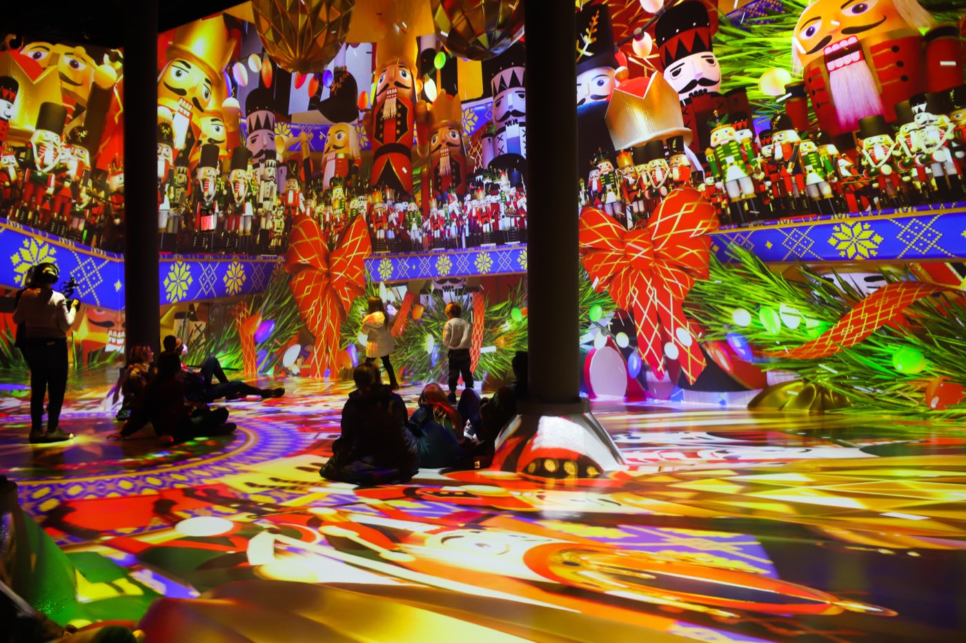 Guests sitting on a floor covered in holiday projections between two steel columns