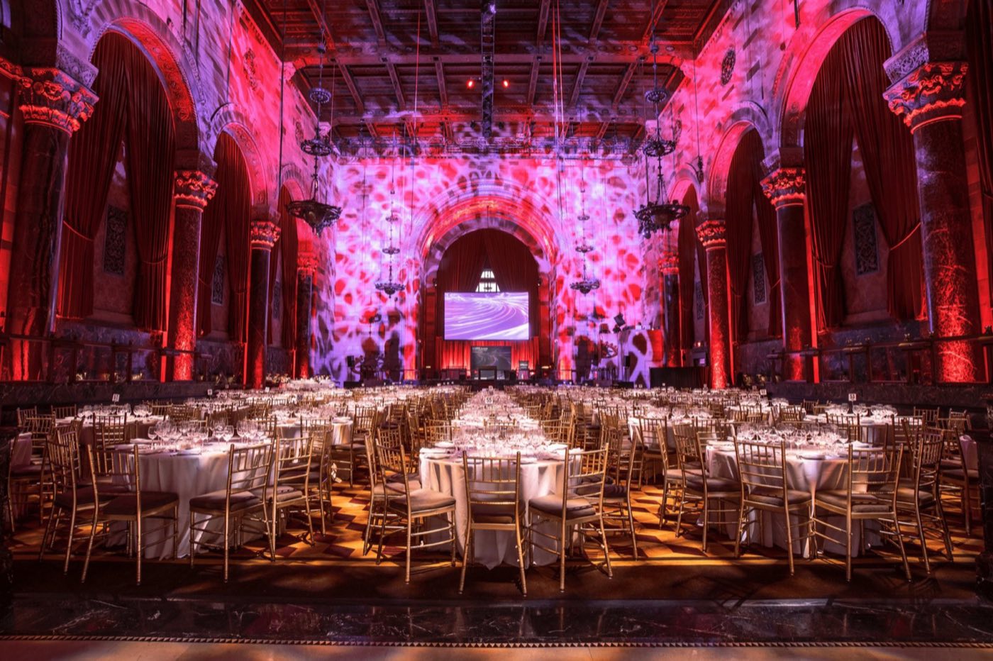 Former bank hall set for a seated dinner with red uplighting and patterned wall projections