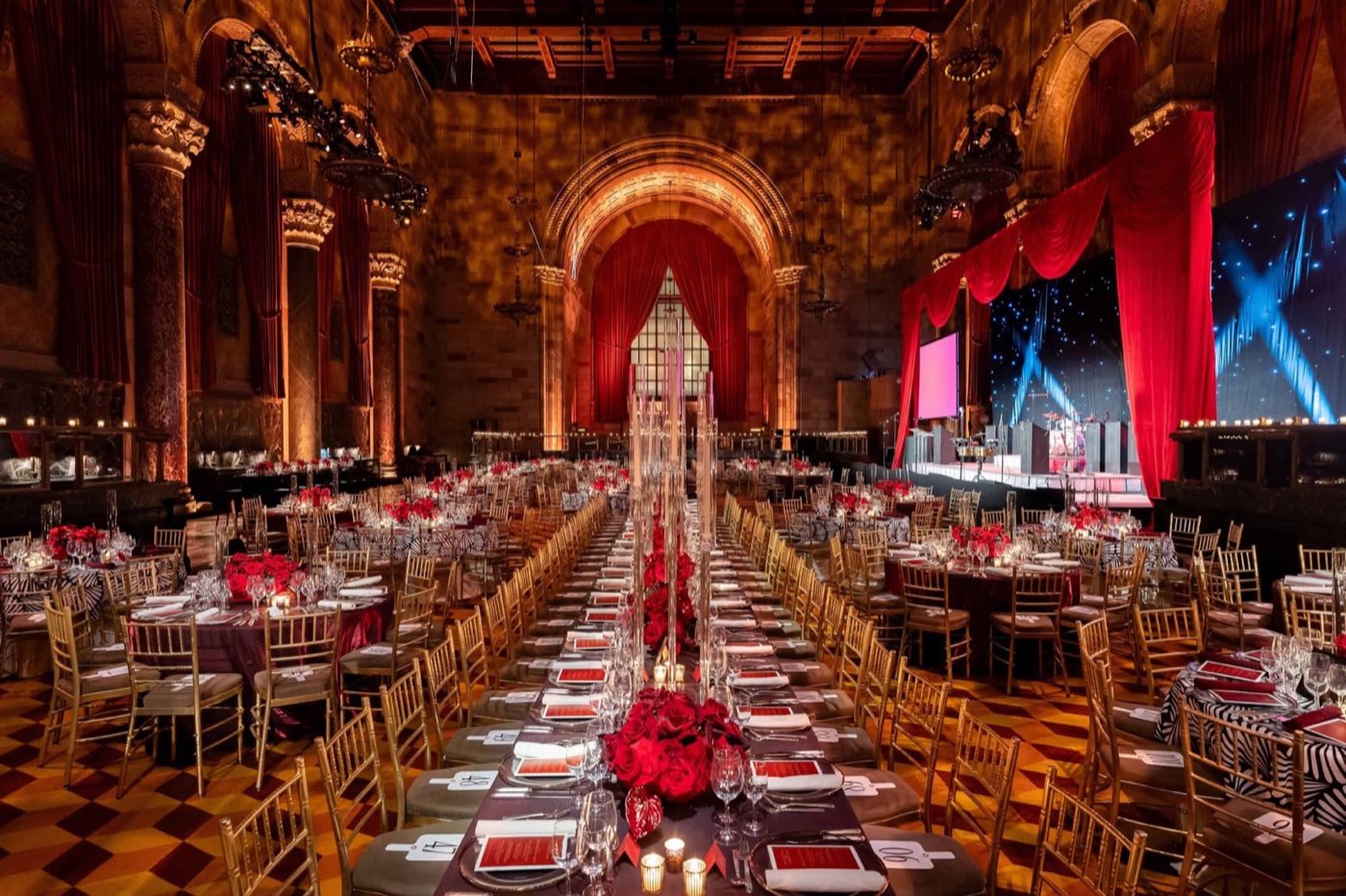 Long banquet tables down the center of the hall with a stage under the arched window