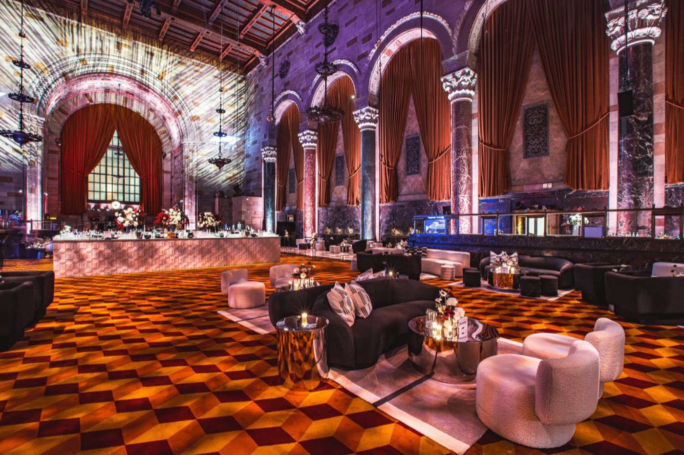 Lounge seating and a central bar set on the patterned carpet under tall arches