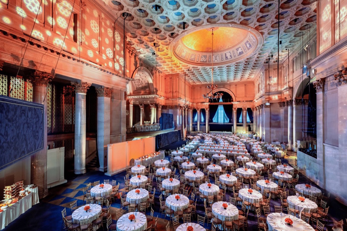 Great hall set with round dinner tables under a coffered dome and tall marble columns