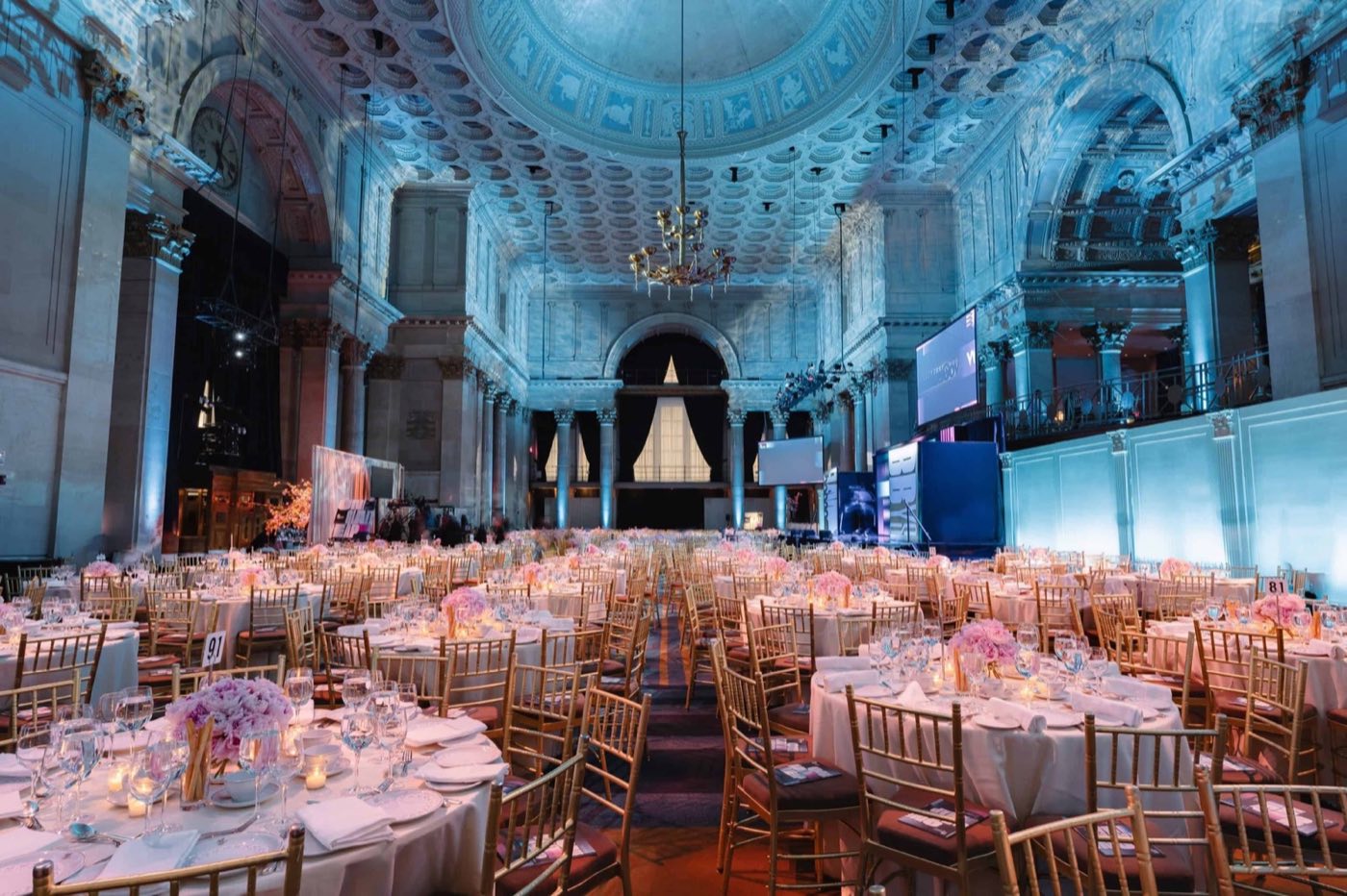 Banquet tables fill the ballroom beneath the coffered ceiling, lit in cool blue tones