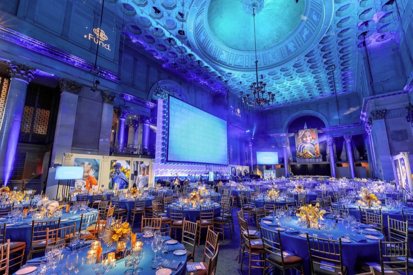 Ballroom dressed for a gala dinner with a large projection screen and blue lighting