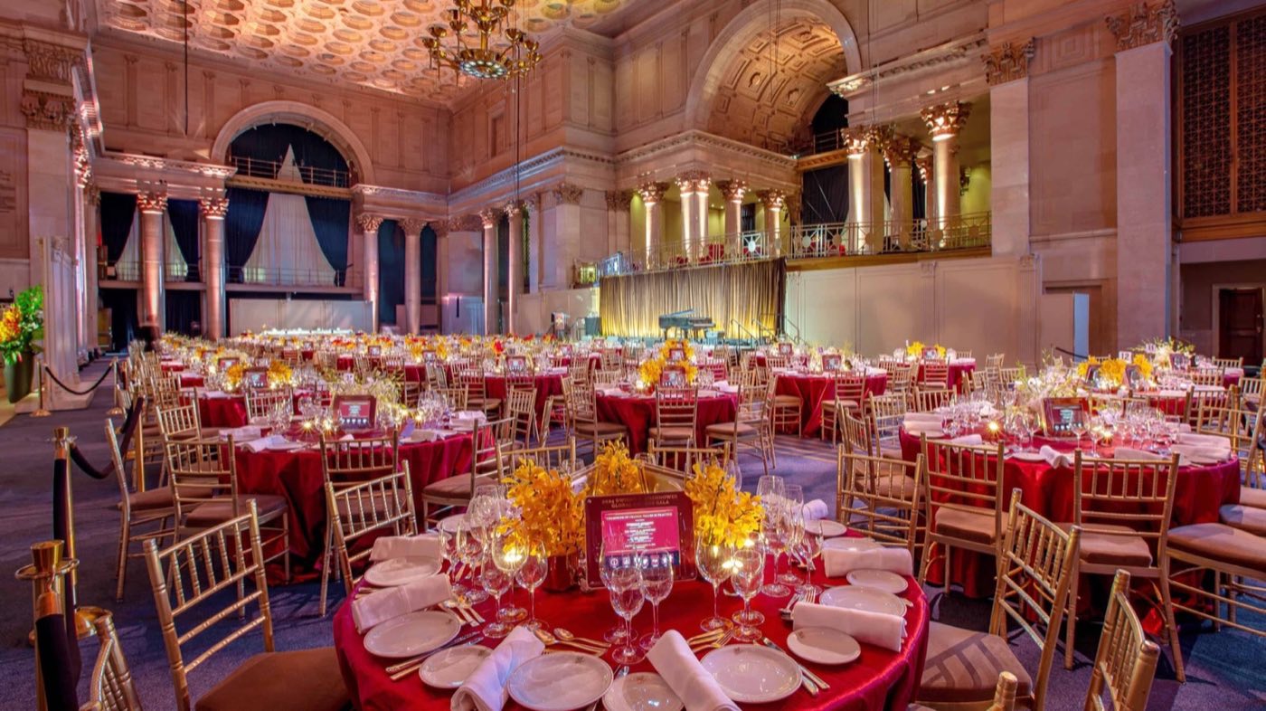 Round tables with red linens and centerpieces set across the columned great hall
