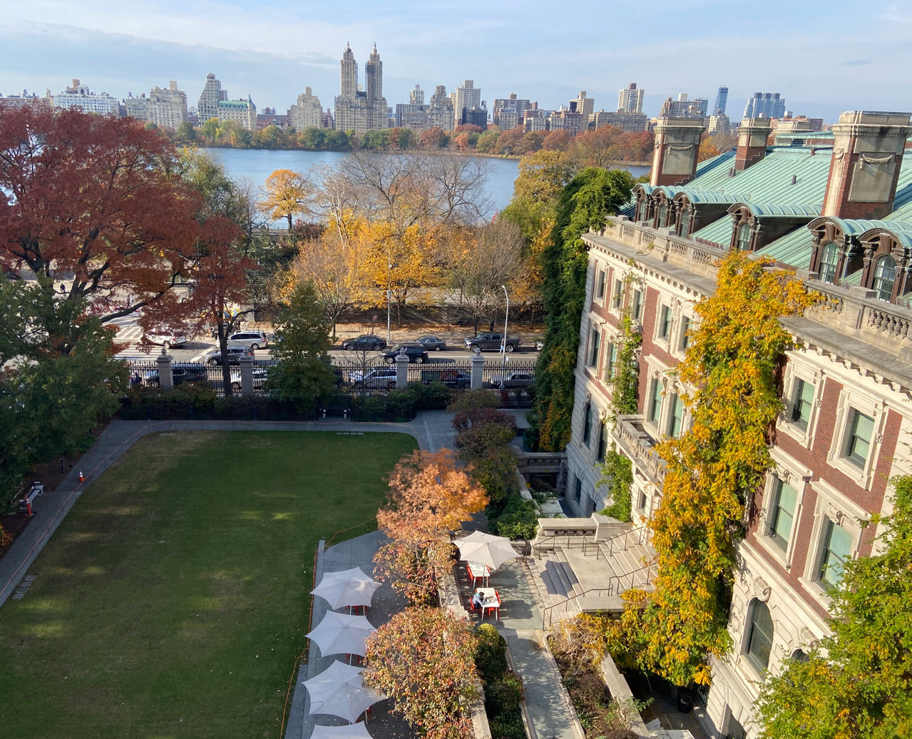Garden lawn with white umbrellas beside the mansion and Central Park reservoir beyond